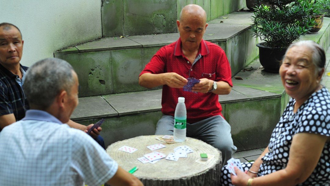 Grupo de idosos jogando cartas ao ar livre, sorrindo durante o jogo