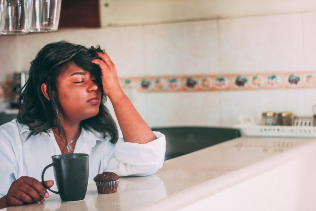 Cuidadora exausta sentada à mesa da cozinha, representando a sobrecarga de quem cuida de um idoso