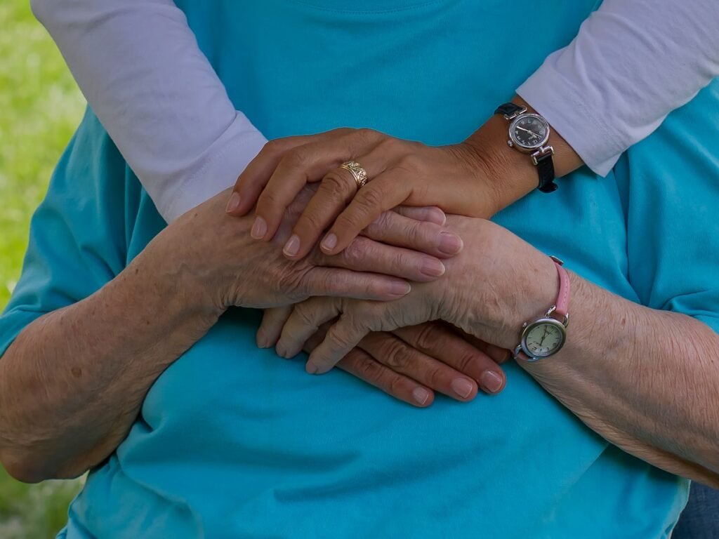 Mãos entrelaçadas em gesto de cuidado entre cuidadora e idosa