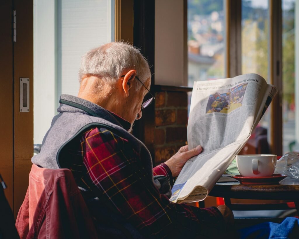 Idoso lendo junto à janela com uma xícara de café ao lado, representando o encaixe da atividade na rotina da manhã
