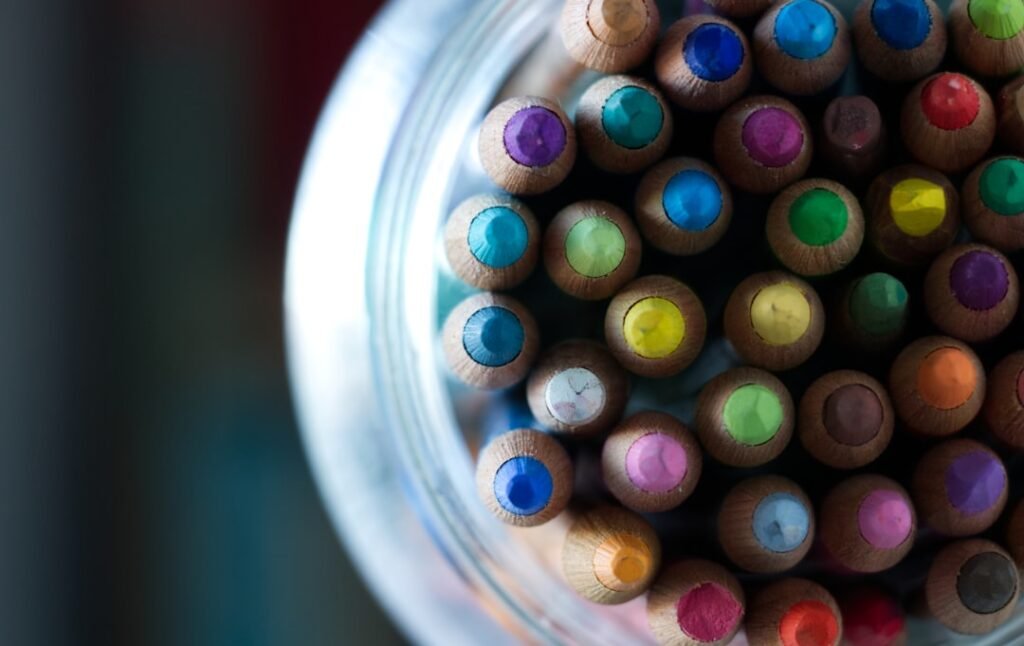 Potinho de vidro cheio de lápis de cor coloridos, vistos de cima, prontos para atividades de colorir