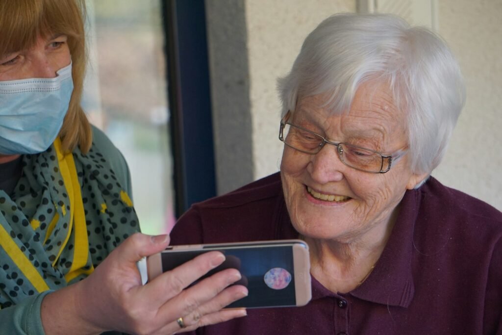 Mulher mostrando a tela do celular para uma senhora idosa, que sorri ao ver a imagem