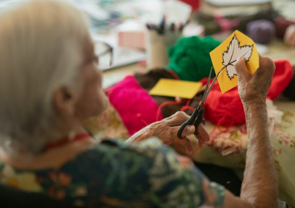 Idosa recortando com tesoura uma folha de outono impressa em papel colorido, atividade manual simples