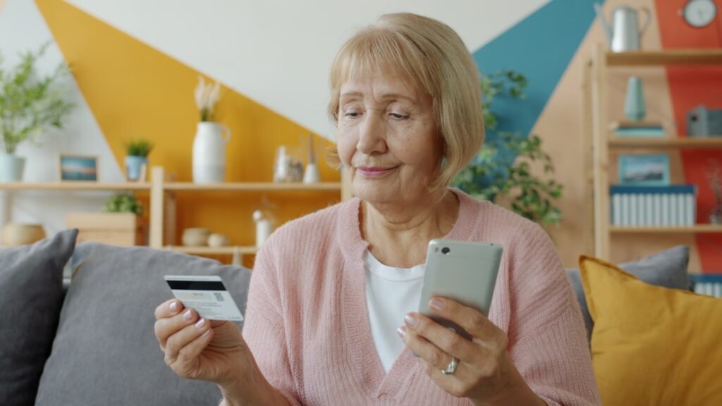 Idosa segurando um cartão em uma mão e o celular na outra, com expressão atenta