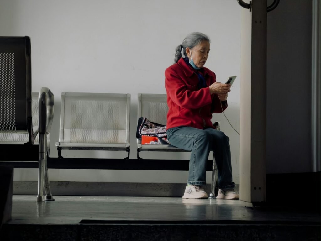 Senhora de casaco vermelho sentada em um banco, usando o celular sozinha