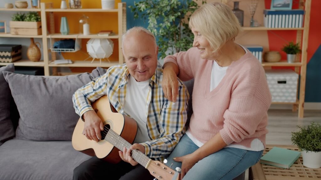 Casal de idosos sorrindo em casa enquanto o homem toca violão
