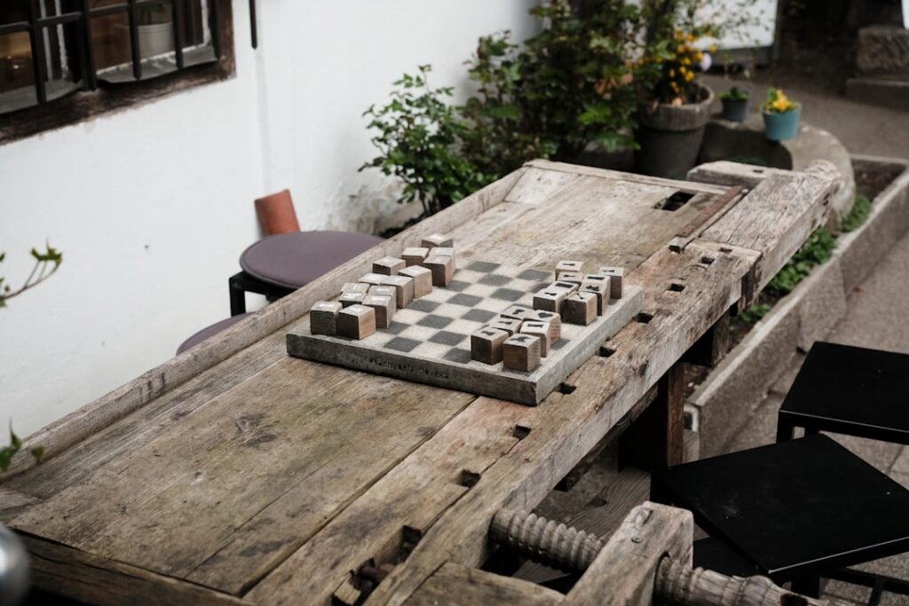 Tabuleiro de damas com peças de madeira grandes sobre uma mesa rústica ao ar livre