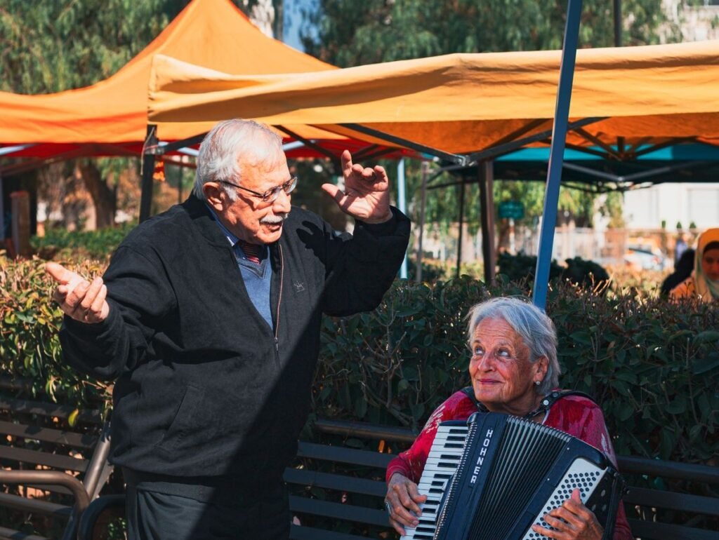 Casal de idosos animado ao ar livre, ela tocando sanfona e ele gesticulando ao cantar